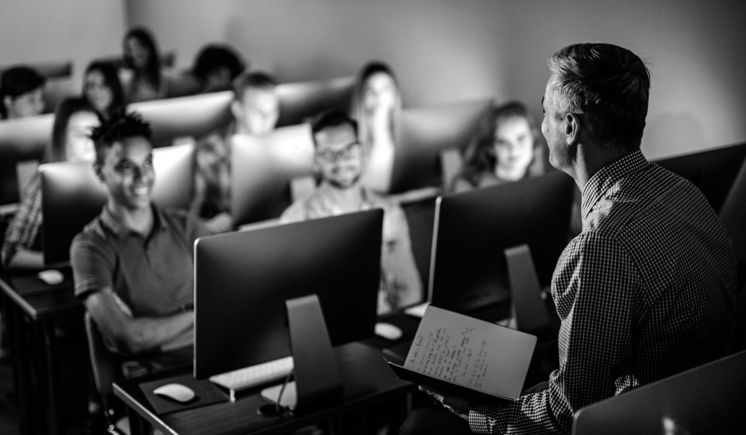 Male teacher talking to large group of students on a class at computer lab.